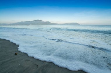 Kıyı kumsalda bulutlu sabah sırasında sıçramasına dalga.