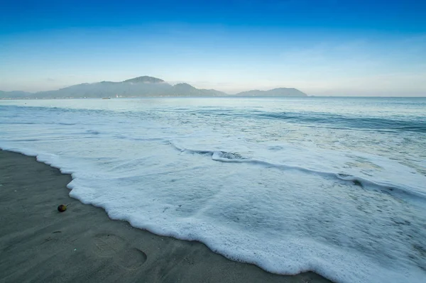 Kıyı kumsalda bulutlu sabah sırasında sıçramasına dalga.