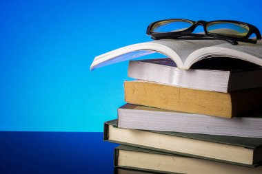 Eğitim kavramı ile yığın eski mavi bir arka plan üzerinde kitap ve okuma gözlükleri.