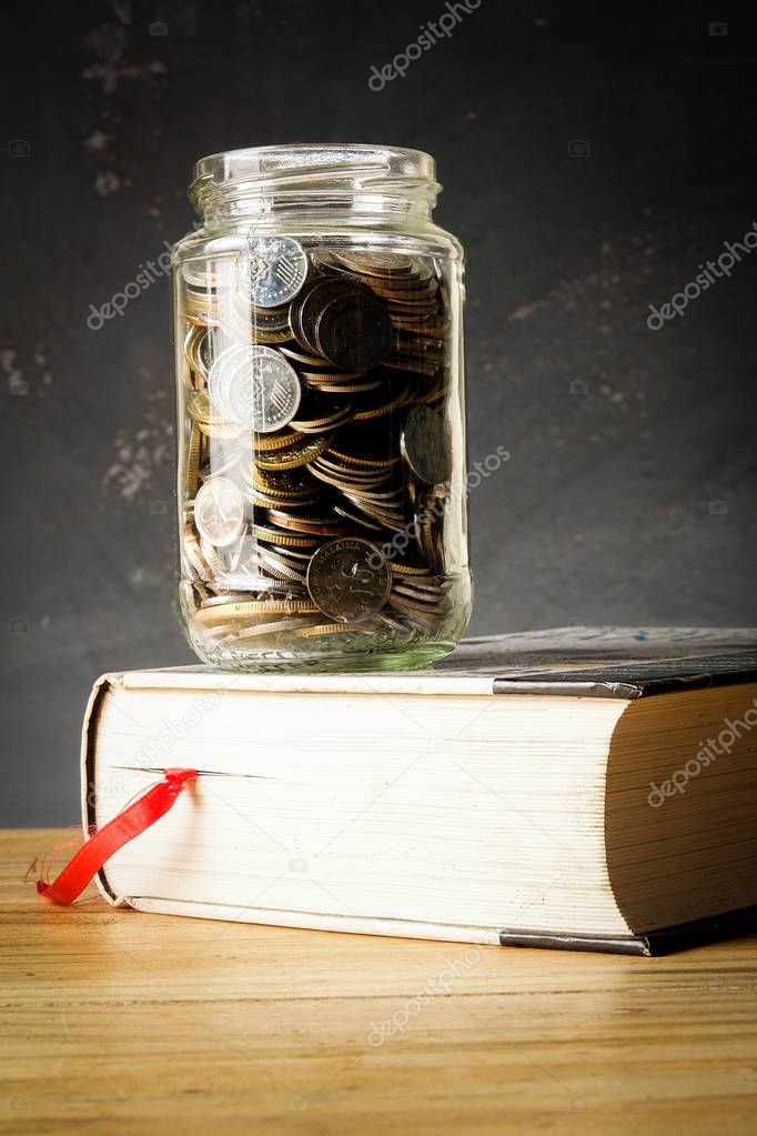 EDUCATION FUND CONCEPT with coins in a glass jar and old book.