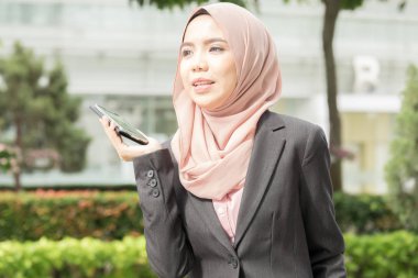 Genç Müslüman kadın kullanım akıllı telefon bir bahçesi.