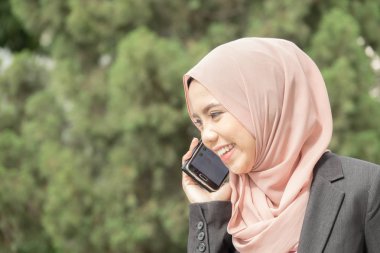 Genç Müslüman kadın kullanım akıllı telefon bir bahçesi.