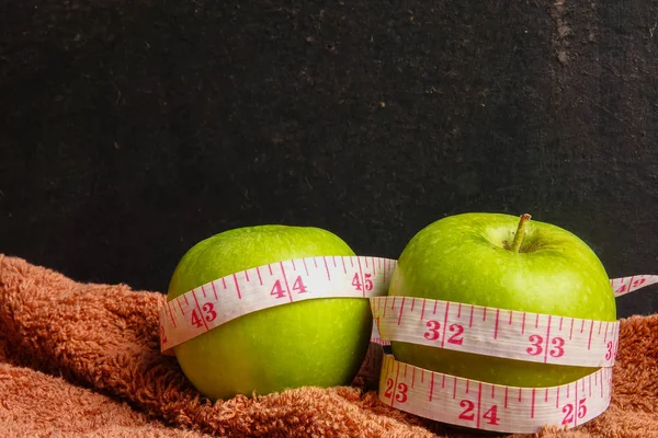 HEALTH LIFESTYLE CONCEPT: Green apples and measuring tape over black rustic background. Selective focus.