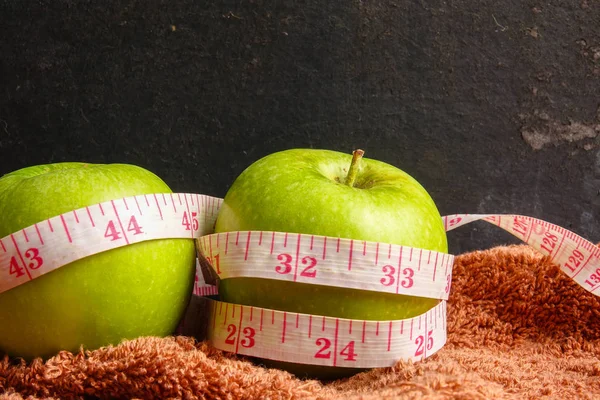 HEALTH LIFESTYLE CONCEPT: Green apples and measuring tape over black rustic background. Selective focus.