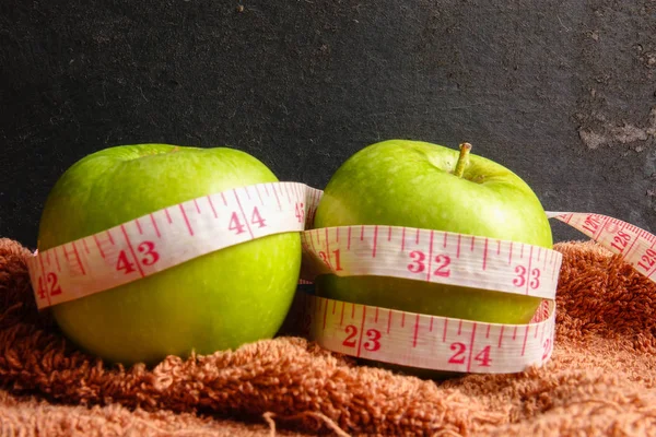 HEALTH LIFESTYLE CONCEPT: Green apples and measuring tape over black rustic background. Selective focus.