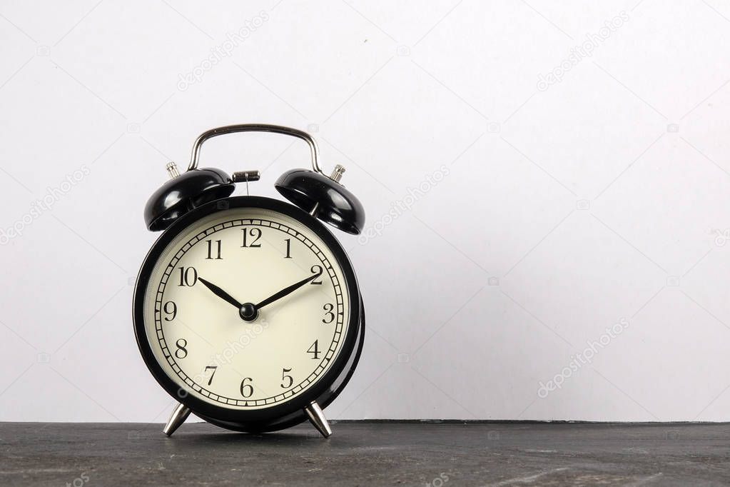 Black alarm clock on the wooden surface against the white background.