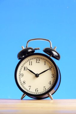 Ahşap yüzey mavi arka plan üzerinde siyah çalar saat.