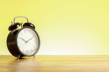 Sarı arka plana karşı ahşap yüzeyde siyah çalar saat.