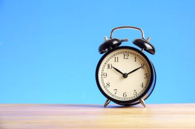 Ahşap yüzey mavi arka plan üzerinde siyah çalar saat.