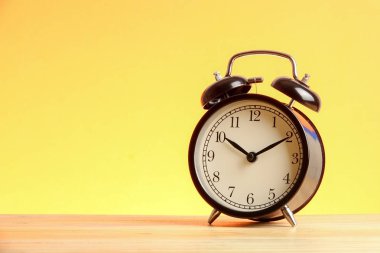 Sarı arka plana karşı ahşap yüzeyde siyah çalar saat.