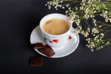 Sabah Kahvesi ve siyah arka planda güzel beyaz çiçekler ve çikolata. Sıcak bir kahvaltı. Düzleştirme biçimi.