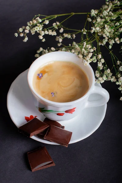Sabah Kahvesi ve siyah arka planda güzel beyaz çiçekler ve çikolata. Sıcak bir kahvaltı. Düzleştirme biçimi.
