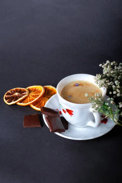Sabah Kahvesi ve güzel beyaz çiçekler, portakallar ve siyah arka planda çikolata. Sıcak bir kahvaltı. Düzleştirme biçimi.