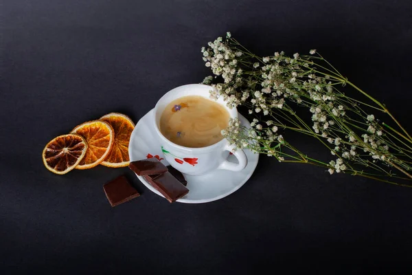 Sabah Kahvesi ve güzel beyaz çiçekler, portakallar ve siyah arka planda çikolata. Sıcak bir kahvaltı. Düzleştirme biçimi.