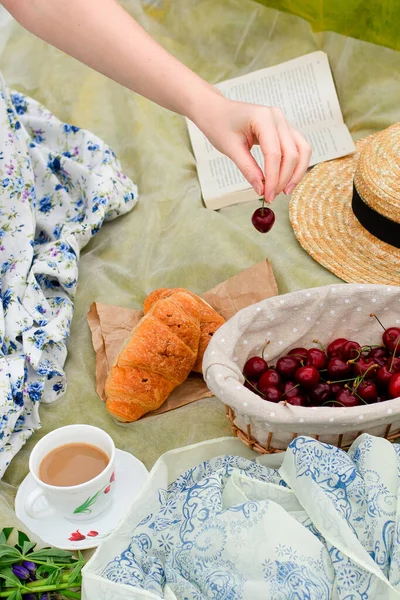Yaz - çayırda piknik. Kız elinde kiraz, tatlı kiraz, kahve, bardakta içecek, çiçek, lupin, kruvasan, çörek, tatlı, şapka, sepet..