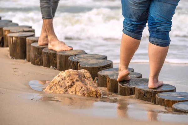 Sandy coast of the Baltic sea. A man and a woman are standing on a log breakwater. A stone lying in the wet sand. — Stock Image Sandy Coast Baltic Sea Man Woman Standing Log Breakwater Stone Royalty Free Stock Photos