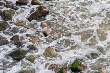 Deniz suyu büyük kıyı kayalarını yıkar. Dalgalar ıslak parlak kayalarda kırılıyor. Suyun dokusu ve kayalık yüzey.