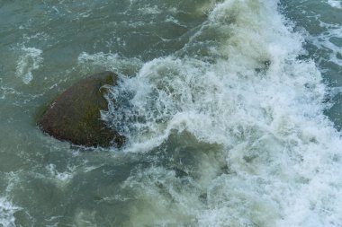 Deniz suyu büyük kıyı kayalarını yıkar. Dalgalar ıslak parlak kayalarda kırılıyor. Suyun dokusu ve kayalık yüzey.