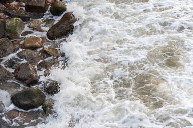 Deniz suyu büyük kıyı kayalarını yıkar. Dalgalar ıslak parlak kayalarda kırılıyor. Suyun dokusu ve kayalık yüzey.