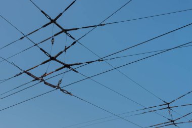 Açık mavi gökyüzünün arka planında, tramvay kablolarının kesiştiği yerde. Enerji transferi için elektrik kablolarını naklet.