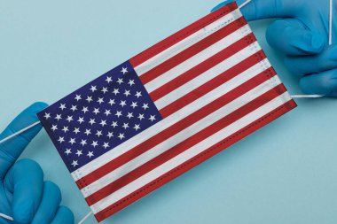 Mavi bir geçmişi olan bir doktorun elindeki Amerikan bayrağı. Coronavirus Covid-19 salgını sırasında ABD 2020 Bağımsızlık Günü.