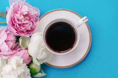 Mavi arka planda beyaz kahve ve beyaz ve pembe şakayık çiçekleri. Romantik bir kahvaltı. Günaydın kavramı.