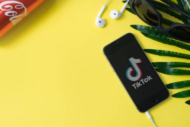 Kirov, Rusya - 28 Haziran 2020: Tik Tok uygulama simgesi akıllı telefon ekranında sarı arka planda bir yaprak, kulaklık ve bir kutu Coca-Cola ile birlikte. Tiktok Sosyal medya ağı. Boşluğu kopyala, düz yat, üst görünüm