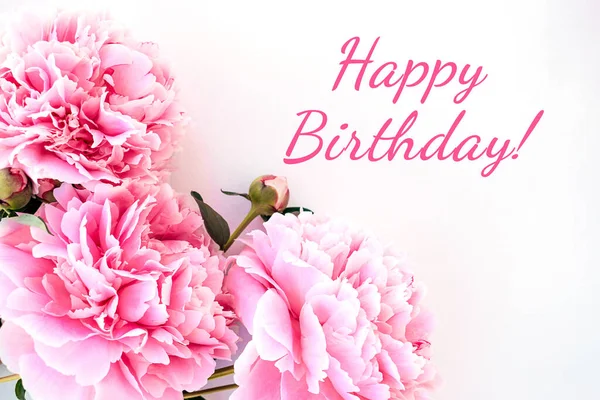 Frame of pink peonies close up and the inscription HAPPY BIRTHDAY on a white background.Birthday greeting card.Selective focus with shallow depth of field