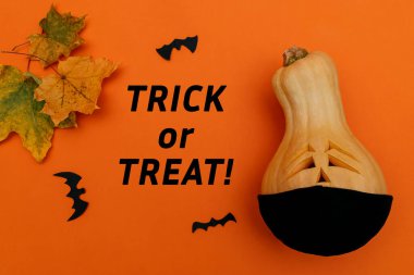 Siyah koruyucu tıbbi maskeli Cadılar Bayramı balkabağı, turuncu arka planda siyah kağıt ve akçaağaç yaprağı yarasaları. Yazı: Hem de turuncu bir arka planda. Cadılar Bayramı ve covid-19 kavramı..