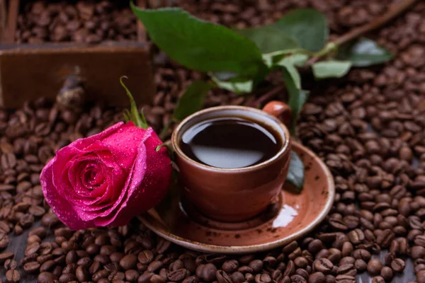 Tasse de café noir et rose sur grains de café torréfiés — Photo