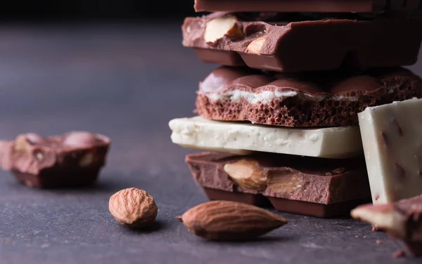 Stapel Dunkler Schokoladenstücke Und Mandeln Auf Dunklem Hintergrund — Stockfoto