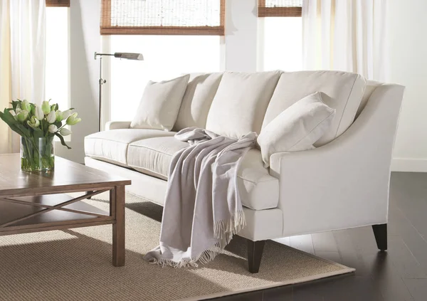 Living room interior with white sofa covered with blanket and flowers on a table. plaid and pillows on a sofa at home. Home cosines.
