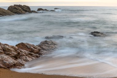 Akşamları dalgalı suyla kumsaldaki kayalar Fransa 'da denizin yüzeyine etki eder..