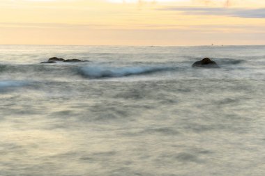 Akşamları dalgalı suyla kumsaldaki kayalar Fransa 'da denizin yüzeyine etki eder..