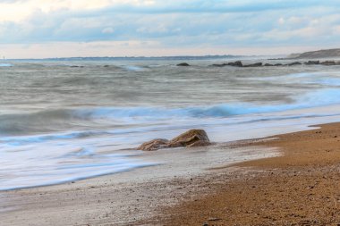 Akşamları dalgalı suyla kumsaldaki kayalar Fransa 'da denizin yüzeyine etki eder..