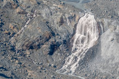 Kayalar ve enkazlarla çevrili, buzullarda çağlayan sular. Bu doğal olay, güneşli bir günde gözlemlenen buzun erimesi sonucu meydana gelir..