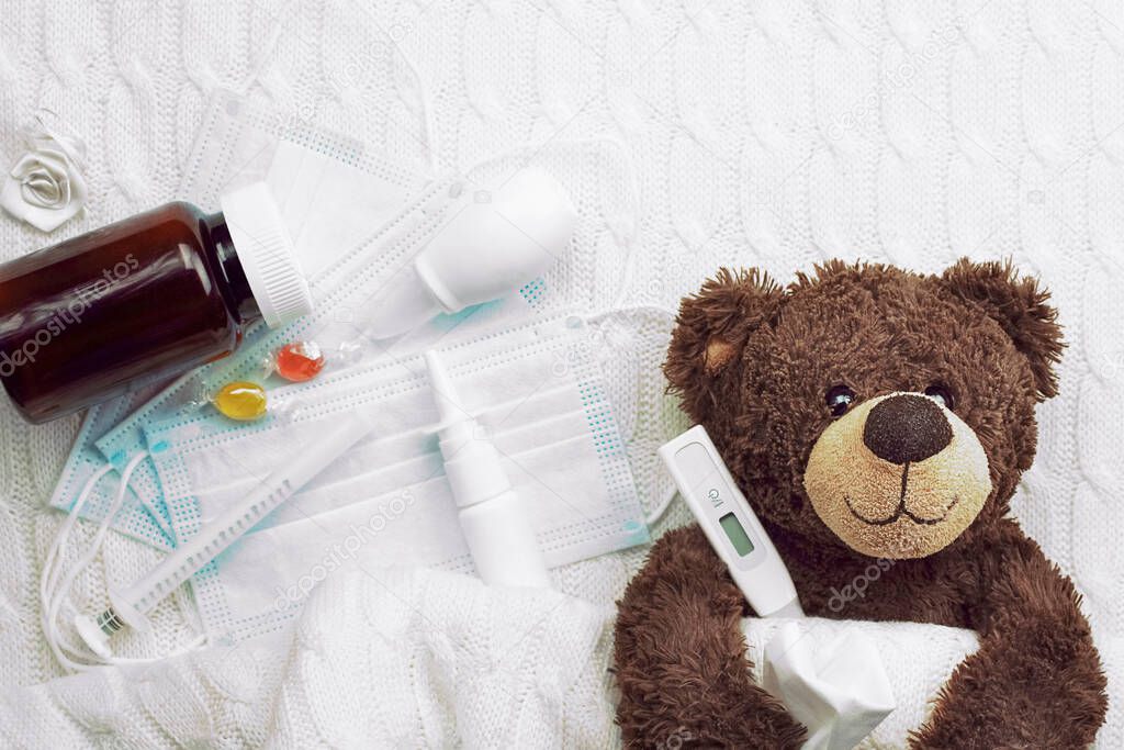 children's brown teddy bear with a thermometer tablets and a medical mask during the pandemic period, children's seosonal diseases . High quality photo