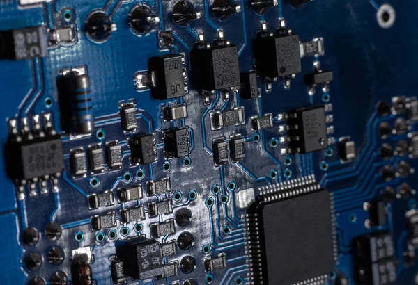 Close-up of a blue printed circuit board (PCB) with stripes of conductors between a transistor and an electronic equipment processor. IT technologies in programming, upgrade and abstract background