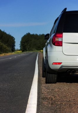 Modern beyaz bir araba yol kenarında yeşil bir tarlanın yanında seyahat ederken ve yeni yollar ararken durur. Hafta sonları, yerel seyahatler ve yaz gezileri.