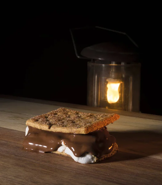 Thick smore on a wood table with a camping lantern burning behind
