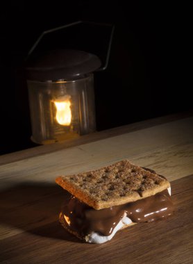 Ahşap bir masa üzerinde bir taze erimiş smore ile aydınlatılmış kamp fener