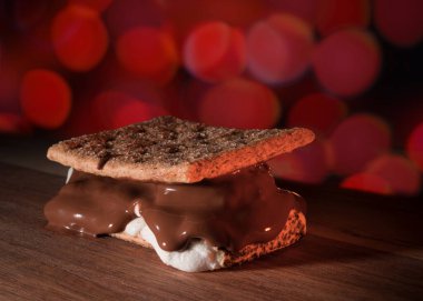 Kırmızı parti ışıkları, ahşap masanın her yerinden sızmaya hazır bir s 'more' un arkasında..