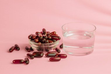 Cam kaseden dökülen iyot, demir ya da vitamin hapları ve pembe arka planda bir bardak suyla sağlıklı yaşam tarzını ve sağlığını destekliyor.