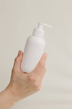 El, minimalist bej arkaplan üzerine pompalı beyaz bir plastik şeker şişesi tutuyor. Kozmetik, krem ya da ilaç için uygun.