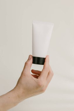 Siyah şapkalı beyaz bir kozmetik tüpü tutan bir kadın. Güzellik ve cilt ürünlerini tanıtıyor.