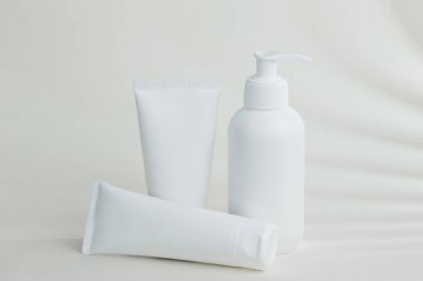 Kozmetik şişeleri ve tüpleri beyaz yüzeyde yaprak gölgesi ile duruyor, markalaşma ve paketleme sunumu için bir model oluşturuyor