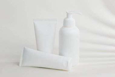 Beyaz masa üzerinde yaprak gölgesiyle duran kozmetik ambalajlar güzellik ve sağlık ürünleri için temiz ve modern bir estetik yaratıyor.