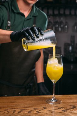 Barmen siyah eldiven giyiyordu. Bardakları karıştırıp, tahta tezgahtaki buzla bardağa parlak sarı kokteyl döküyordu.