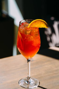 Buz küpleri ve portakal dilimli canlı portakal kokteyli, ahşap bir masada saplı bir bardakta sunuluyor, sıcak güneş ışığının tadını çıkarıyor.