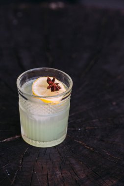 Yeşil kokteyl limon dilimi ve yıldız anasonuyla süslenir. Kırsal ahşap bir masada zarif bir bardakta servis edilir ve şık ve davetkar bir atmosfer yaratır.